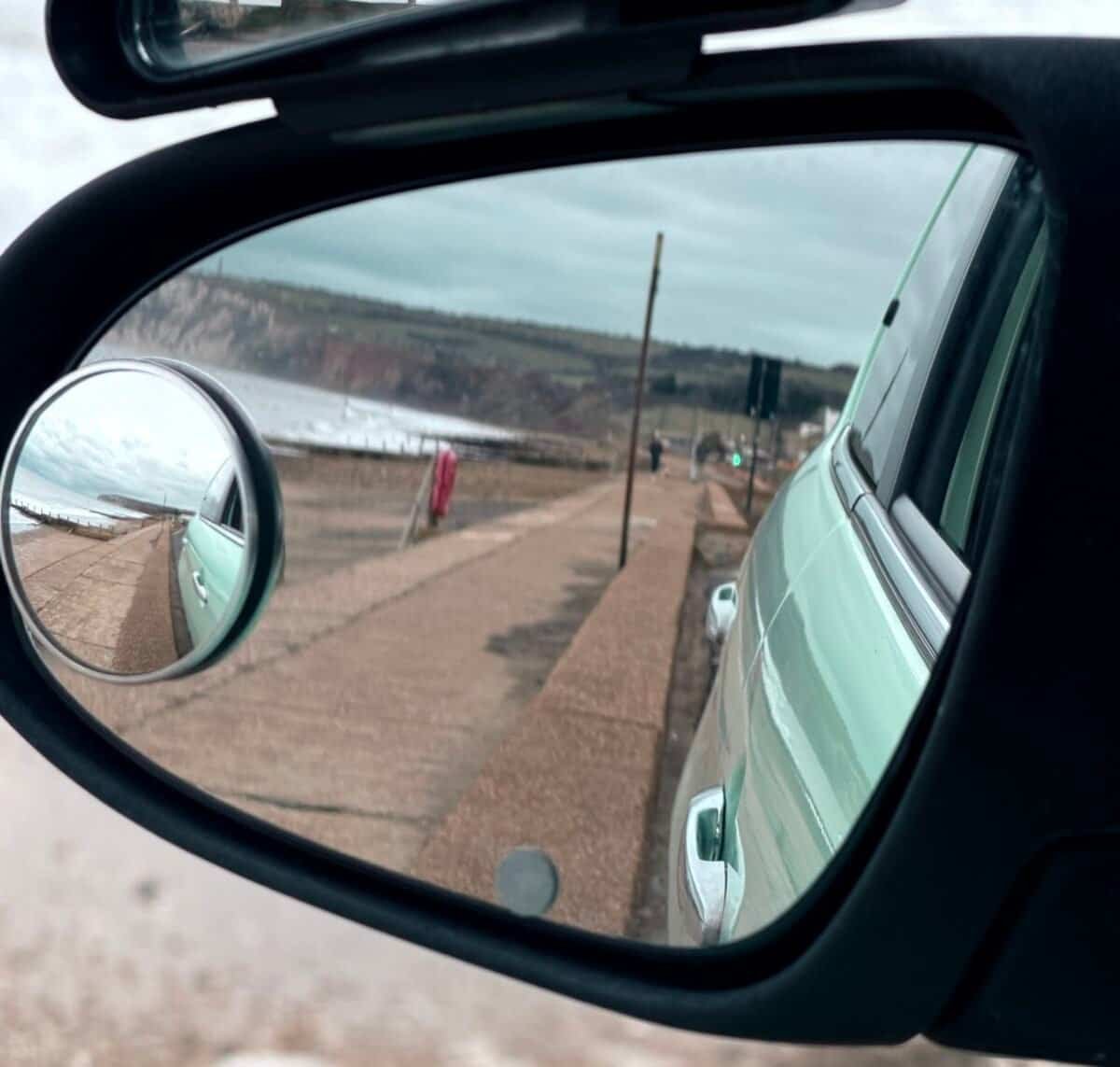 Nearside (left) wing mirror and blind-spot mirror showing the area alongside and behind the car, demonstrating how drivers set the mirror before driving.