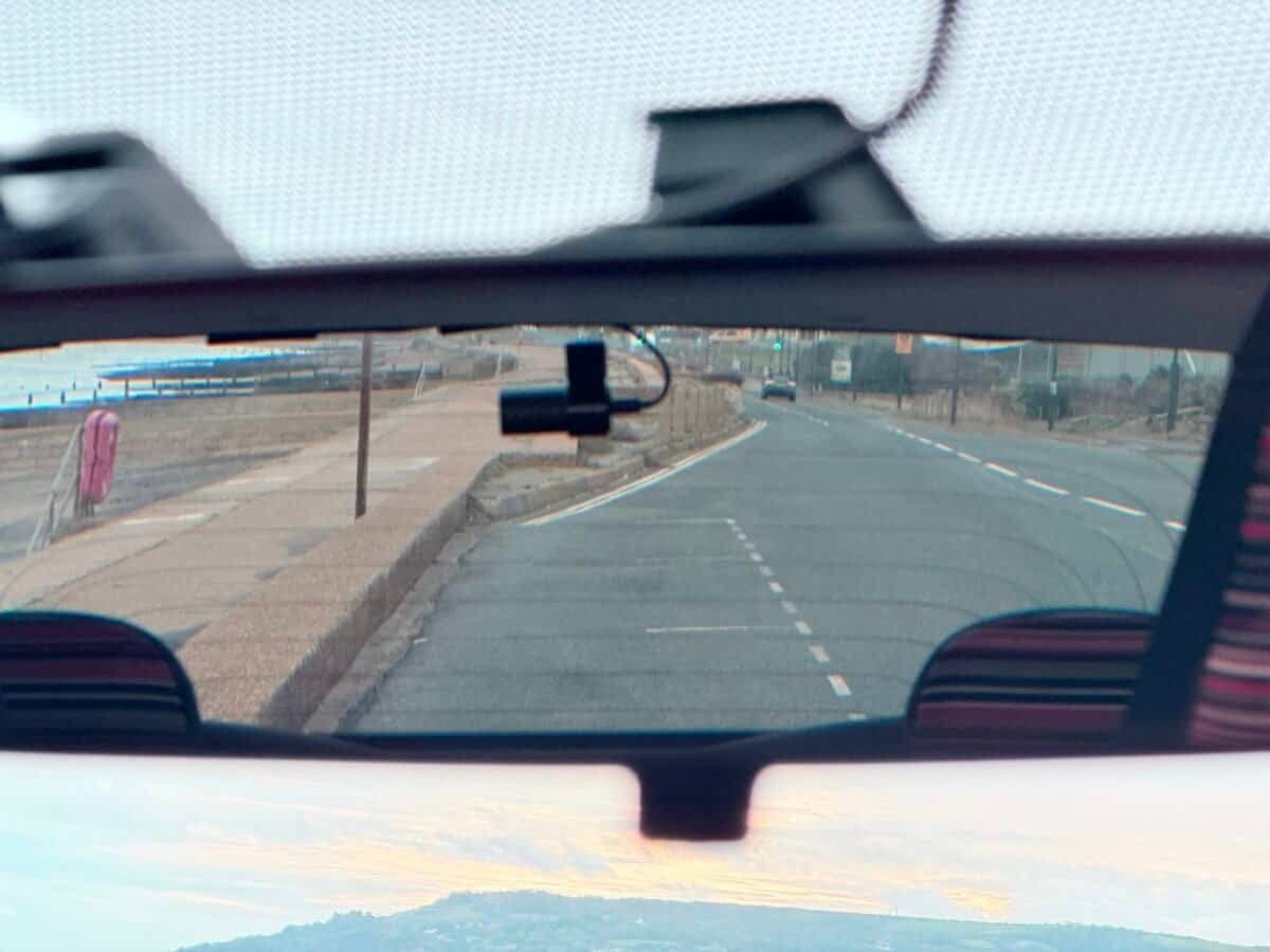 Rear-view mirror showing the road behind the car, illustrating how drivers monitor traffic using interior mirrors.